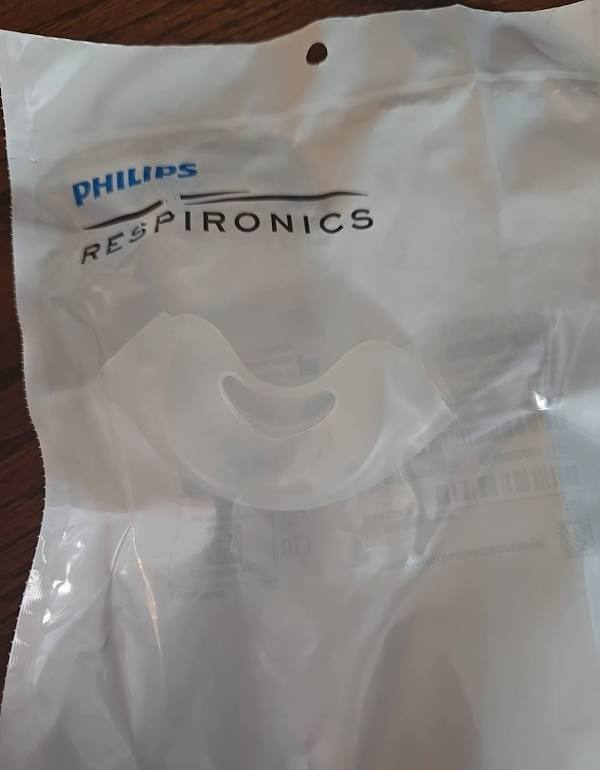 A sealed Philips Respironics nasal cushion in its unopened factory packet. The silicone is clear and colourless.