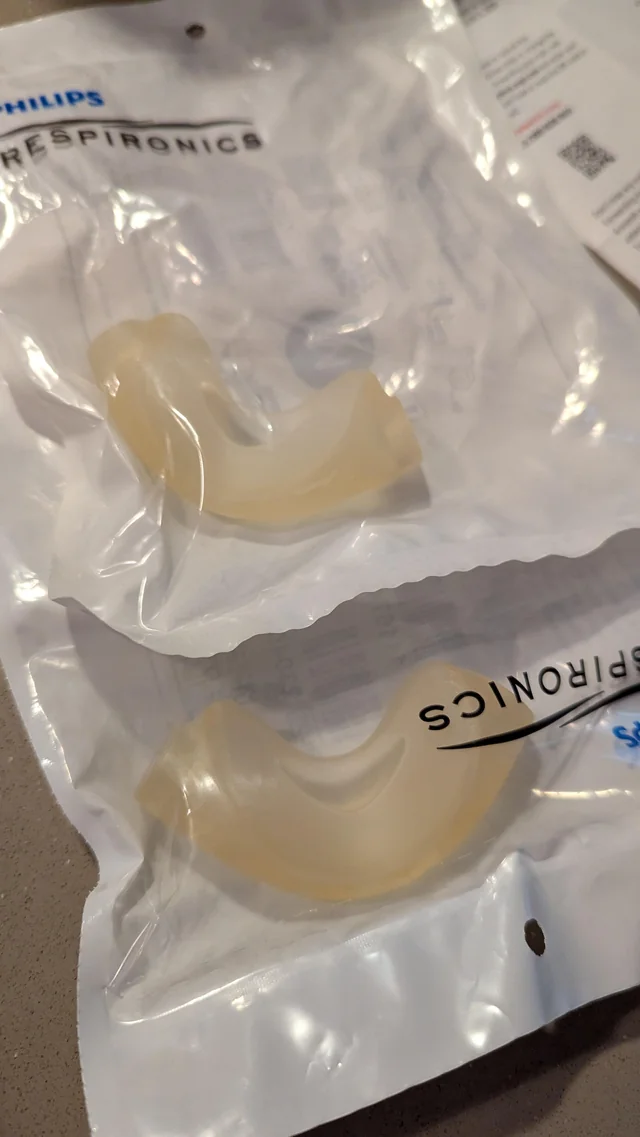Two sealed Philips Respironics cushions in their unopened factory packets. Both have turned an even amber colour with age.